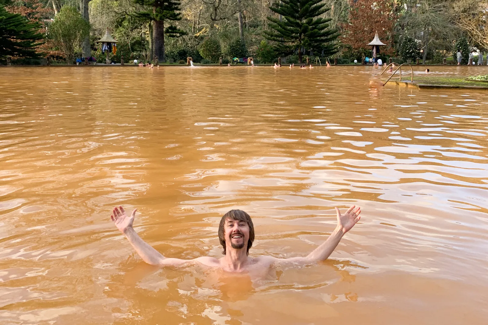 Ein Badender im eisenhaltigen, braunen Wasser eines Thermalbeckens in Furnas