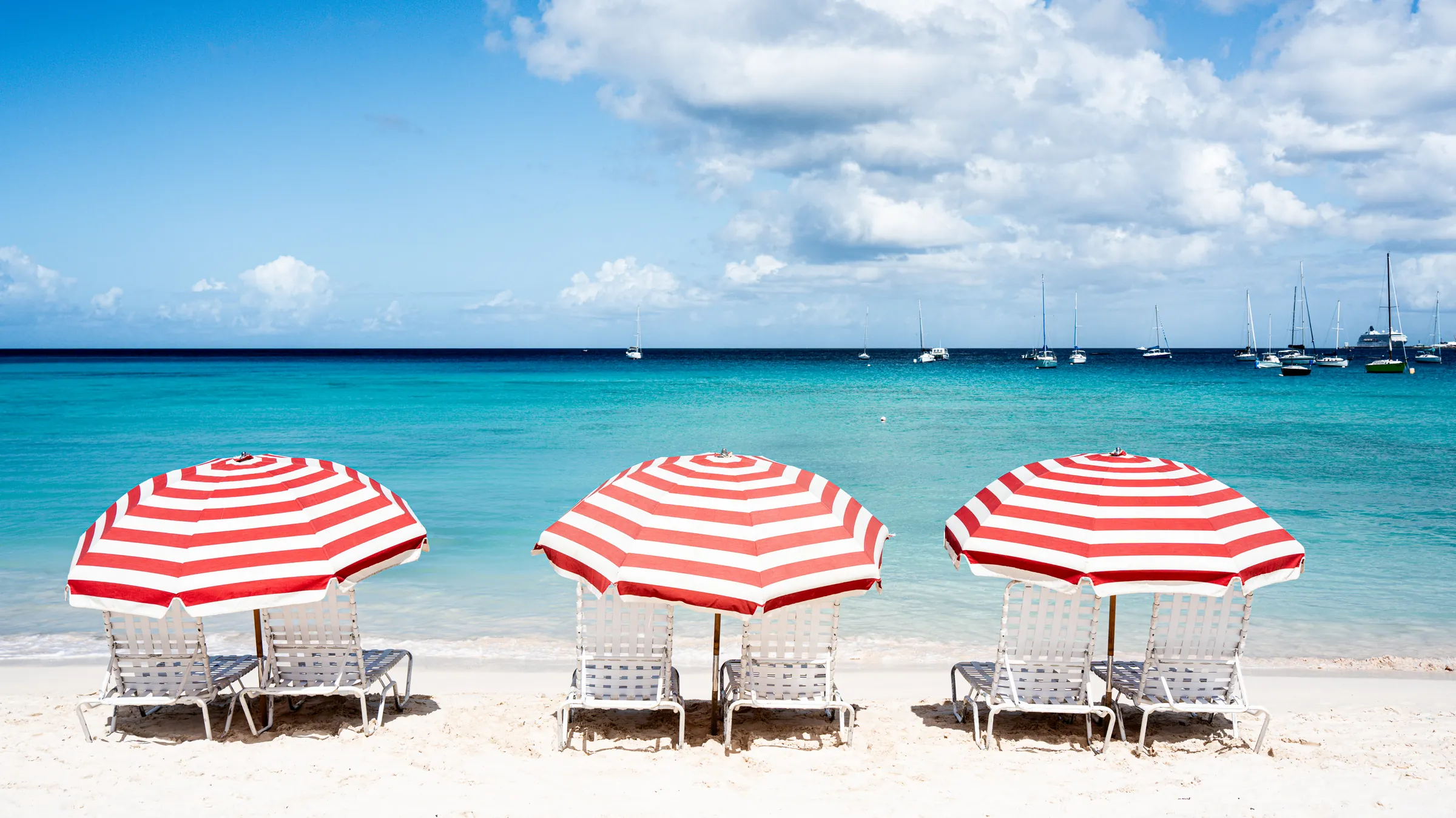 Strand mit rot-weißen Sonnenschirmen und türkisfarbenem Meer auf Barbados