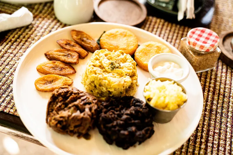 Teller mit kreolischem Frühstück: Kochbananen, Fischküchlein, Rührei und Bohnen