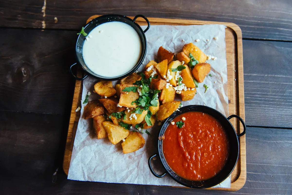 Patatas bravas mit Aioli und scharfer Tomatensauce auf einem Holzbrett