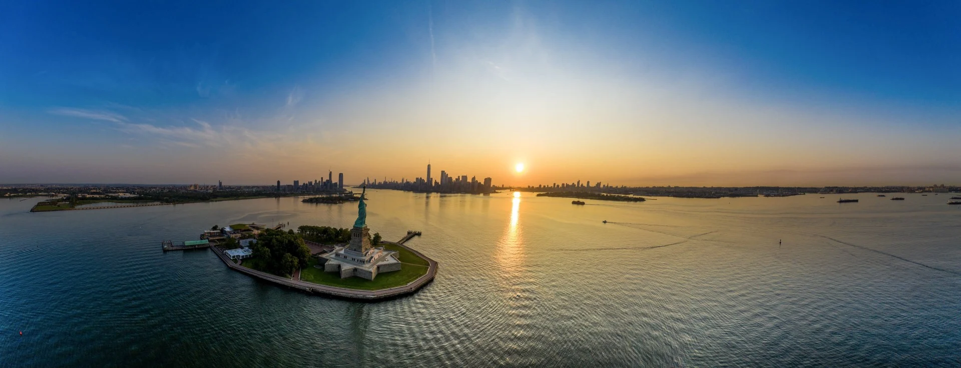 Die Freiheitsstatue vor der Skyline von Manhattan bei Sonnenuntergang aus der Luft