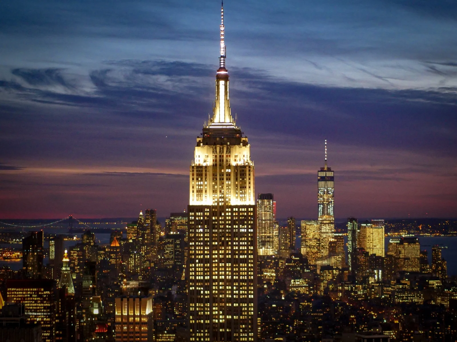 Das beleuchtete Empire State Building bei Nacht, dahinter Lower Manhattan