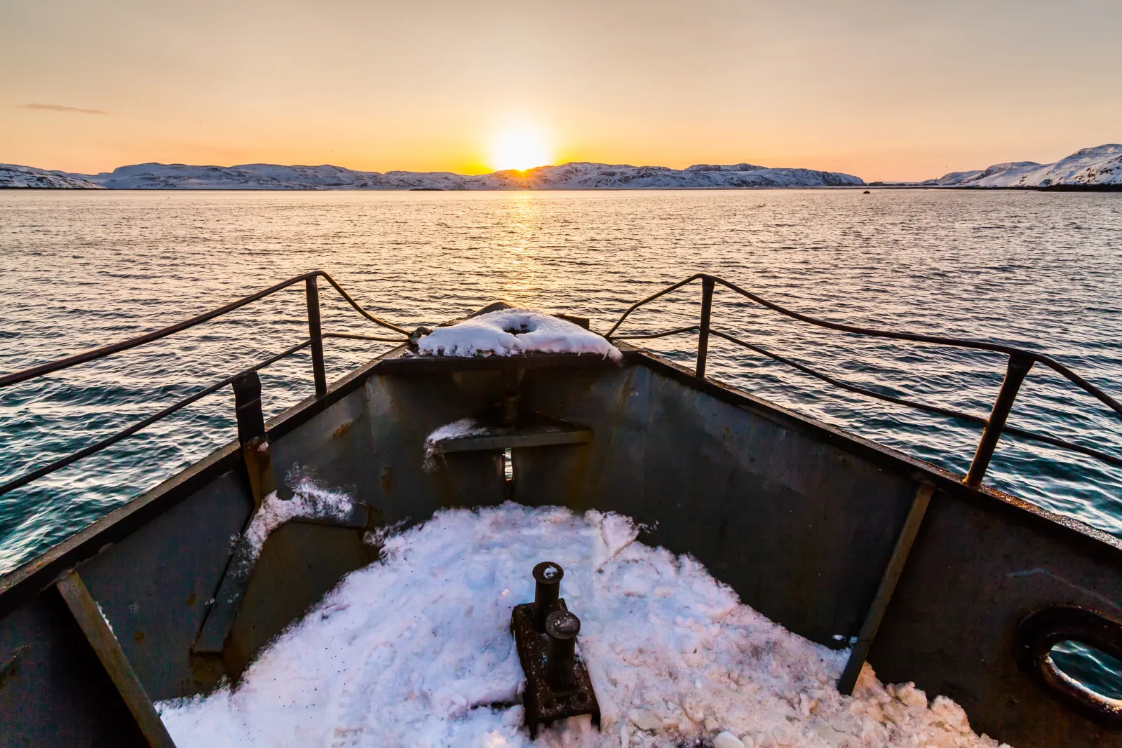 Tiefstehende Sonne über dem Meer, gesehen von einem schneebedeckten Boot